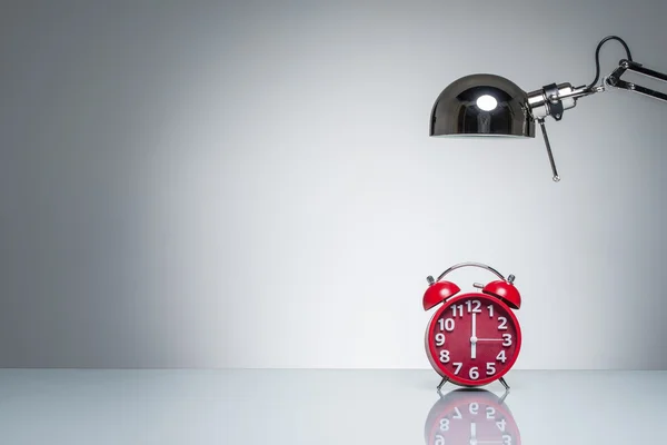 Lighting up red alarm clock with desk lamp — Stock Photo, Image