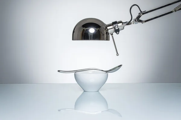 Verlichting van witte ceramische kom zilveren lepel met bureaulamp — Stockfoto