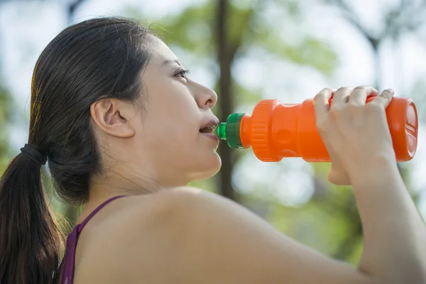 Sporty young asian woman drinking water in the park — Stock Photo, Image