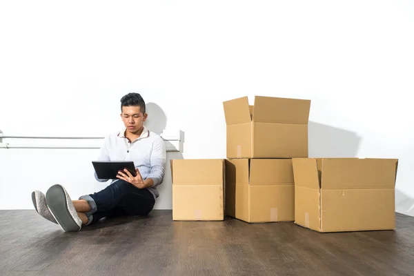 Asiático hombre sentado en el suelo usando su Tablet con cajas —  Fotos de Stock