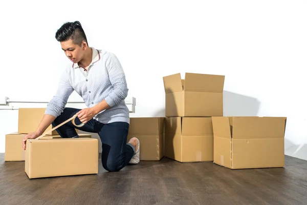 Jonge Aziatische man bewegende huis verpakking karton met behulp van lijm — Stockfoto