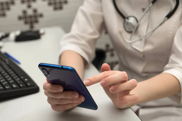 Tıbbi teknoloji konsepti. Hastanenin modern ofisinde cep telefonu ve steteskopla çalışan bir doktor..