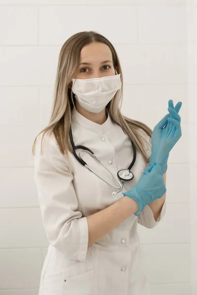 Female doctor in medical mask on the face and gloves on a white background, vertical photo.