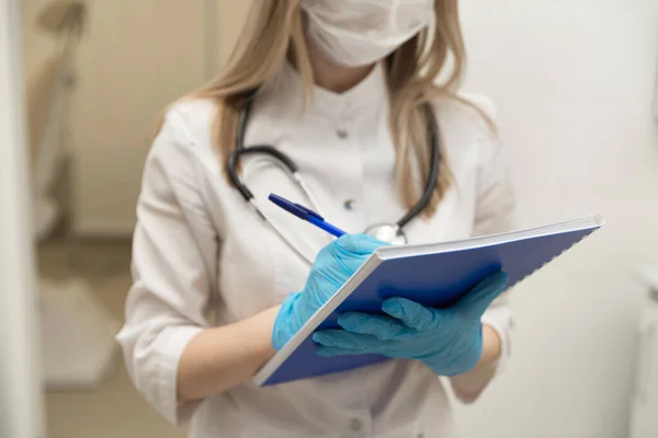 Female doctor filling out medical document. Young woman physician with stethoscope prescribing treatment to patient. Female doctor with pen writing recipe on clipboard in hospital. Close up.