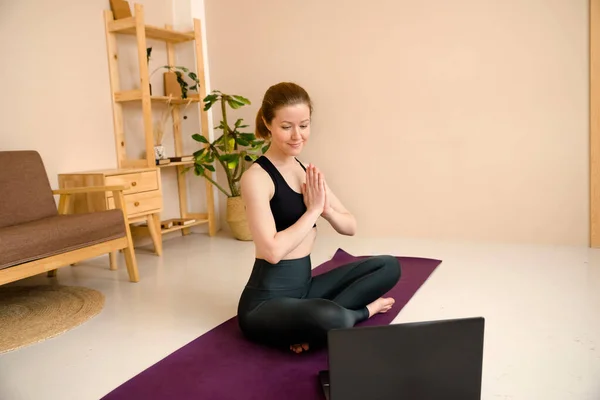 Spor giyimli, laptoplu hoş bir kadın evde dinlenirken yoga yapıyor. Sağlık konsepti, online yoga.