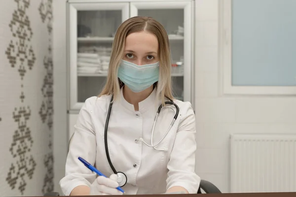 Steteskoplu doktor kadın elinde kalemle masasında oturuyor..