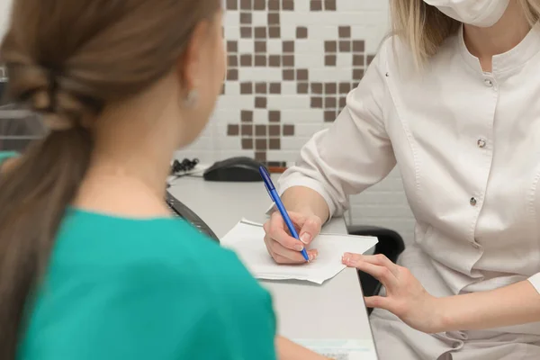 Kadın doktor, ofisteki hastaya reçeteli tedavi teşhisi yazıyor, yakın plan. Sağlık kavramı.