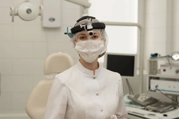 Kadın-doktor-otolaryngolog modern bir hastanede kameraya beyaz önlük ve maskeyle bakıyor..