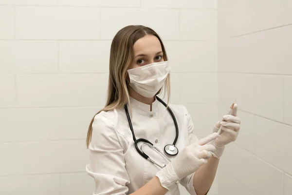 Koruyucu tıbbi maskeli kadın doktor elinde şırınga tutuyor. Sağlık hizmetleri kavramı.