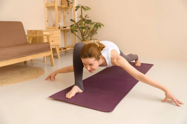 Atletik, kızıl saçlı, orta yaşlı, spor giyimli bir kadın. Oturma odasında spor yapıyor. Spor ve eğlence konsepti.