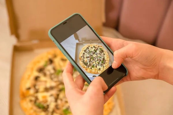 Female hand making a photo of pizza, with a mobile phone in the House, vertically