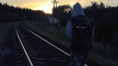 Günbatımında demiryolunda yürüyen yalnız bir kapüşonlu gezgin.