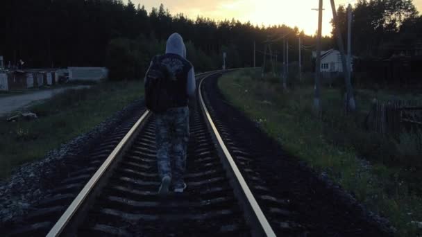 Un voyageur solitaire à capuchon marchant sur le chemin de fer au coucher du soleil — Video