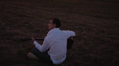 Gün batımında dışarıda gitar çalan yalnız bir adam.