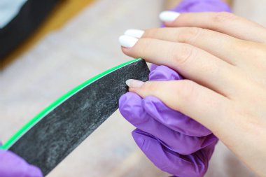 Manikürcü, tırnak törpüsü takan genç bir kadından eski bir manikürü çıkarıyor.