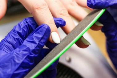 Manikürcü, tırnak törpüsü takan genç bir kadından eski bir manikürü çıkarıyor.