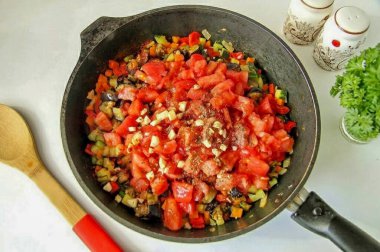 Sonra kızarmış patlıcanları geri ver, kabuklu domatesleri, doğranmış sarımsağı, tuzu ve baharatı geri koy. Havyarı deneyebilirsiniz, eğer ekşiyse, sonra 1-2 tutam şeker ekleyin. Her şeyi karıştır ve 5 dakika daha pişir..