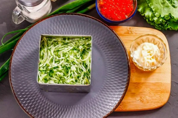 Rinse the fresh cucumber in water, cut the tails off the vegetable and grate into a separate container. Salt and let the slices sit for 5 minutes - it will release the liquid. Squeeze the cucumber out of the liquid and place in a ring or square.