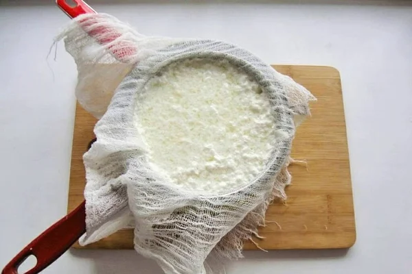 When the whey becomes completely transparent, pour the contents of the pan into a sieve with cheesecloth, folded in several layers. Place the sieve in a deep bowl or saucepan so that the whey flows into it without touching the cheese. Tie the ends of