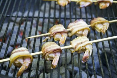 Pastırma dilimlerini kağıt havluya koyun, yağları eritmek için 1,5-2 dakika peçete ve mikrodalga fırınla kaplayın. Her karidesi bir dilim pastırmaya sarın. Daha önce suya batırılmış bir şişte karidesi şiş..