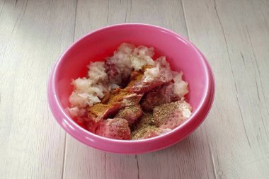 Dövülmüş eti bir kaseye aktarın. Rendelenmiş soğan, barbekü baharatları ve kırmızı biber ekle. Her şeyi birbirine karıştır..