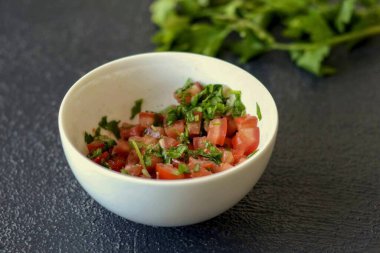 Domatesleri küp küp doğra. Yeşillikleri ince ince doğra. Tadına limon suyu, zeytinyağı, sarımsak ve tuz ekle..