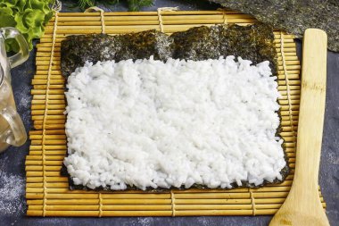 Örtüyü paspasın üzerine koy. Haşlanmış pirinci yosunların üstüne koy, ellerini suya sok. Yukardan 2 cm doldurma, nori bir rulo gibi yuvarlanır. Dikkatli hizala.