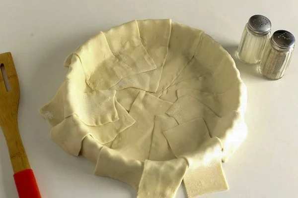 The dough must be defrosted, rolled out and cut into strips. Grease a baking dish with butter and overlap the strips slightly. Press the joints carefully so that the juice from the filling does not flow out during the baking process.