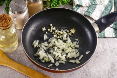 Soğan ve sarımsak soy, suda durula. Soğanın yarısını küp küp doğra, sarımsağı ütüle ya da doğra. Her iki kesiği de sebze yağıyla tavaya dök. Yaklaşık 2-3 dakika kızart.