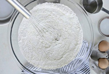 Şimdi mangırı yap. Kabartma tozunu un, tuz ve beyaz şekerle at. Sonra yoğurdun, kalan yağın ve yumurtaların içine dökün. Tekrar karıştır.