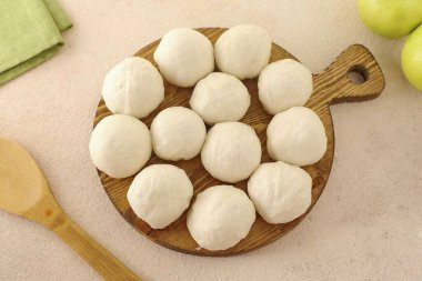 Hamur geldiğinde yoğur ve 12-16 parçaya böl. Her bir hamur parçasını topa dönüştür, onları havluyla ört ve 20 dakika otur..