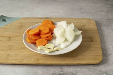 Havuçları yıka, soy ve daireler çiz. Soğanı dörde böl. Sarımsağı soy, karanfili ikiye böl.