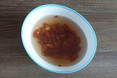 Bademlerin üzerine kaynar su dök ve 10 dakikalığına ayrıl. Ceviz ya da fındık kullanıyorsanız, tavada hafifçe kurutun..