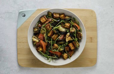 Tofu, patlıcan, bezelye filizi ve domatesleri büyük bir kasede birleştirin. Yavaşça karıştır. Üstü giyinik.