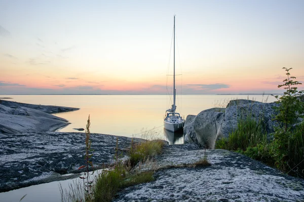 Sailboat moored long side a small rocky island — Stock Photo, Image