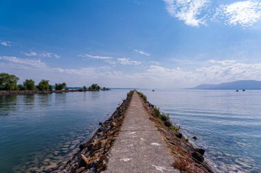 Neuchatel Gölü 'ndeki La Tene' nin JP68752-Rıhtımı İsviçre 'deki Neuchatel Gölü' ndeki Tene deniz fenerine giden uzun bir hendeğin manzarası. Mavi gökyüzü gölün sakin suyuna yansıyor..