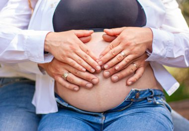 Hamile çiftin, eşlerinin göbeğinin üstüne ellerini koyması. Gelecekteki ebeveyn elleri kalp şeklinde katlanmış..