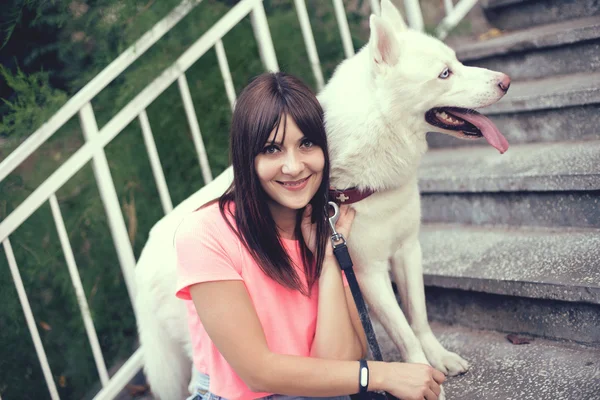 Chica sentada en las escaleras y jugando con su perro husky — Foto de Stock