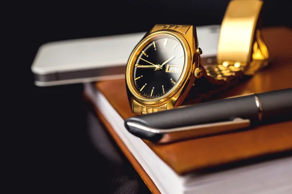 Mens accessory, golden watch, pen and mobile phone on the leather diary.