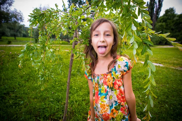 Szczęśliwa dziewczynka pokazano jej język w parku — Zdjęcie stockowe