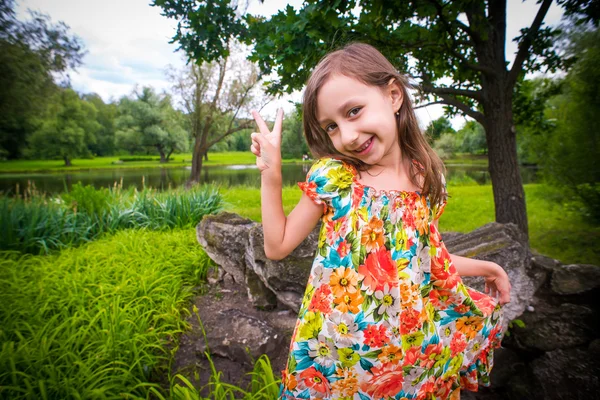 Felice bambina divertendosi i il parco e mostrando segno di pace — Foto Stock
