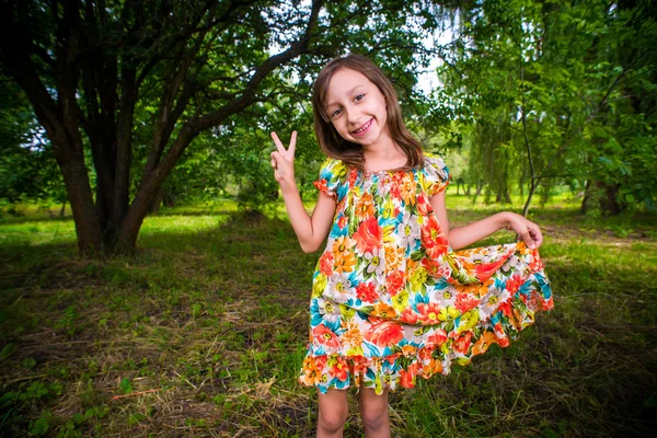 Feliz niña divirtiéndose en el parque y mostrando la señal de paz — Foto de Stock