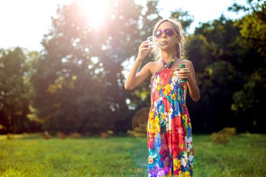 Sevimli küçük kız bir sabun köpüğü yeşil çimenlerin üzerinde esiyor