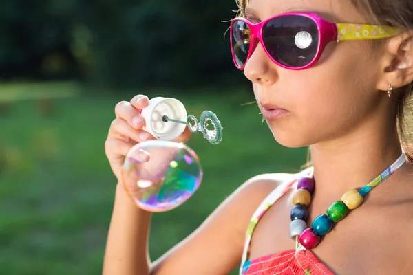 Linda niña está soplando una burbuja de jabón en la hierba verde — Foto de Stock