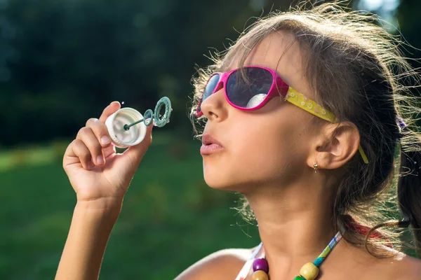 Linda niña está soplando una burbuja de jabón en la hierba verde — Foto de Stock