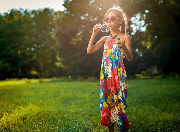 Sevimli küçük kız bir sabun köpüğü yeşil çimenlerin üzerinde esiyor — Stok fotoğraf