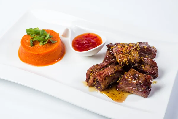 Barbecued pork ribs served with tomato sauce and carrot puree  isolated on white background — Stock Photo, Image