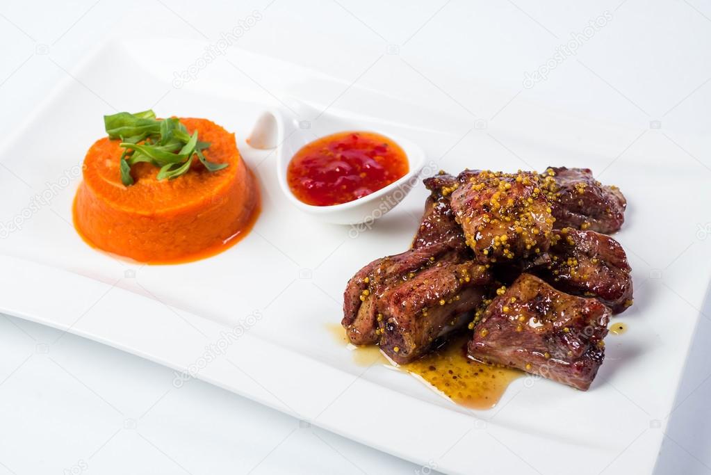 Barbecued pork ribs served with tomato sauce and carrot puree  isolated on white background