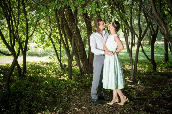 Pareja de boda, hermosa novia joven y el novio de pie en un parque al aire libre tomados de la mano, sonriendo — Foto de Stock