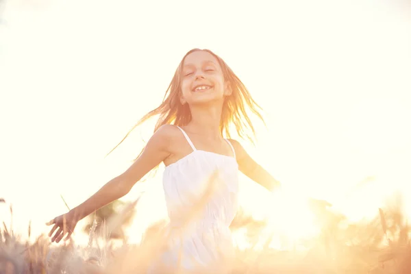 Menina feliz brincando no campo de trigo no pôr do sol — Fotografia de Stock